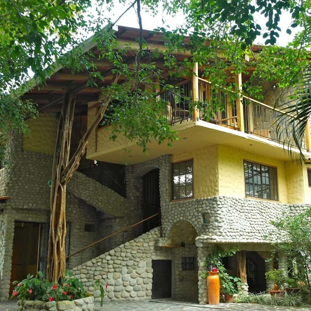 La fachada de Casa di Pietra: estuco amarillo, muros de piedra de río y un árbol que sube hasta el balcón