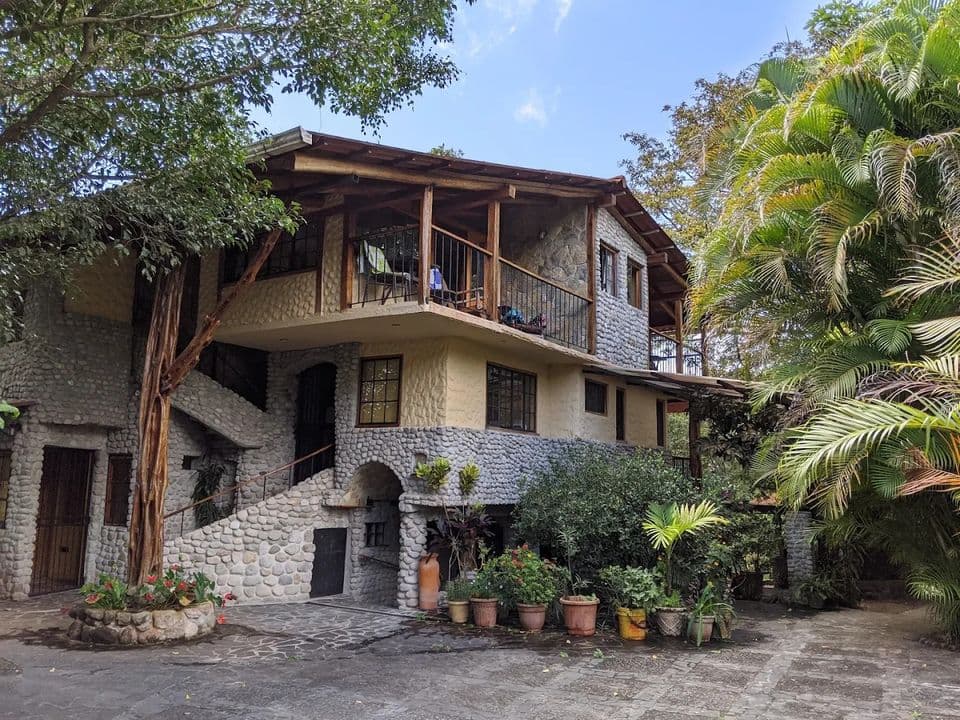 La casa completa entre palmeras y macetas de barro, bajo un cielo azul