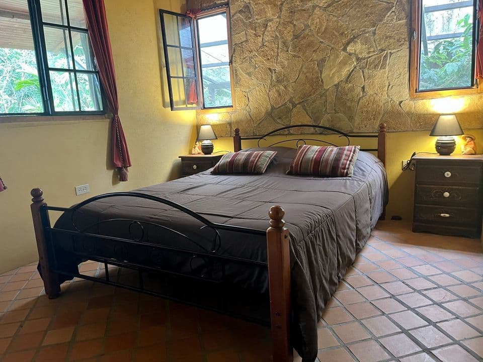 La cama matrimonial frente a la pared de piedra, con lámparas encendidas