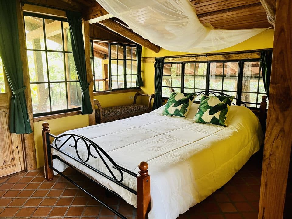 La cama con mosquitero y ventanales hacia el jardín