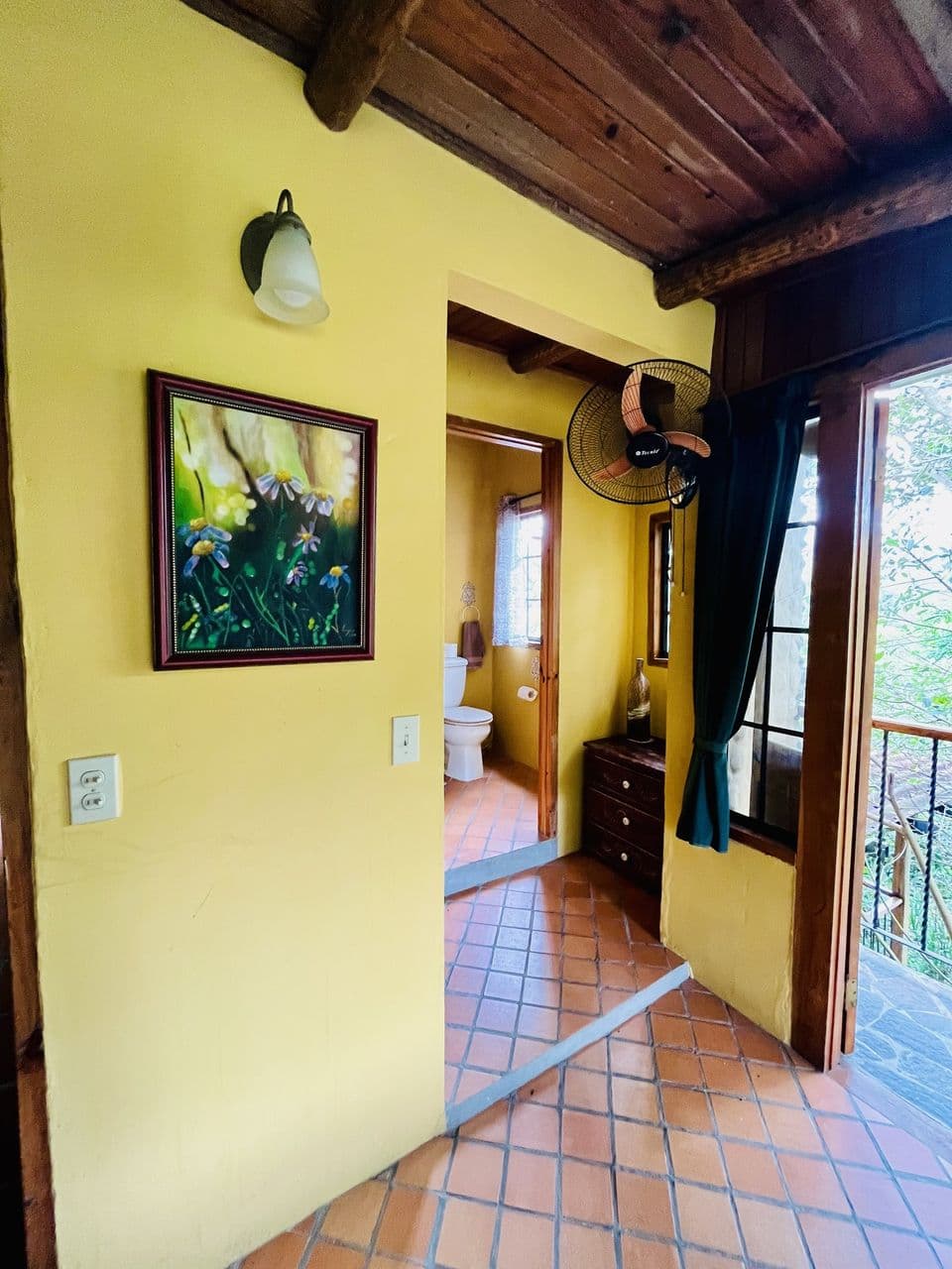 La entrada con ventilador, el baño y la puerta al balcón
