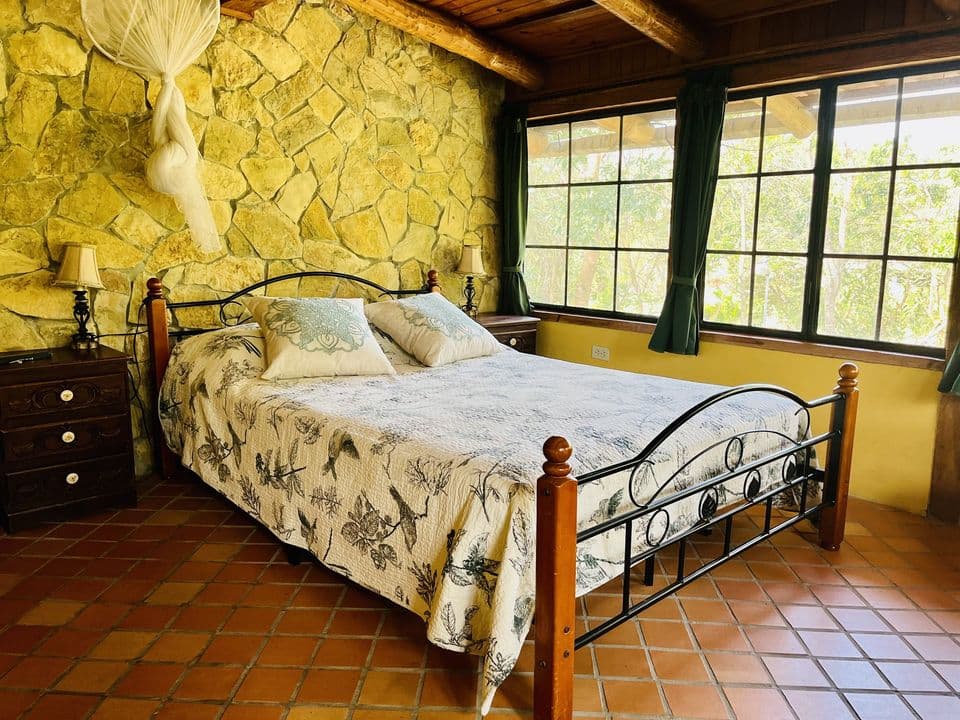 La cama frente a los ventanales y la pared de piedra